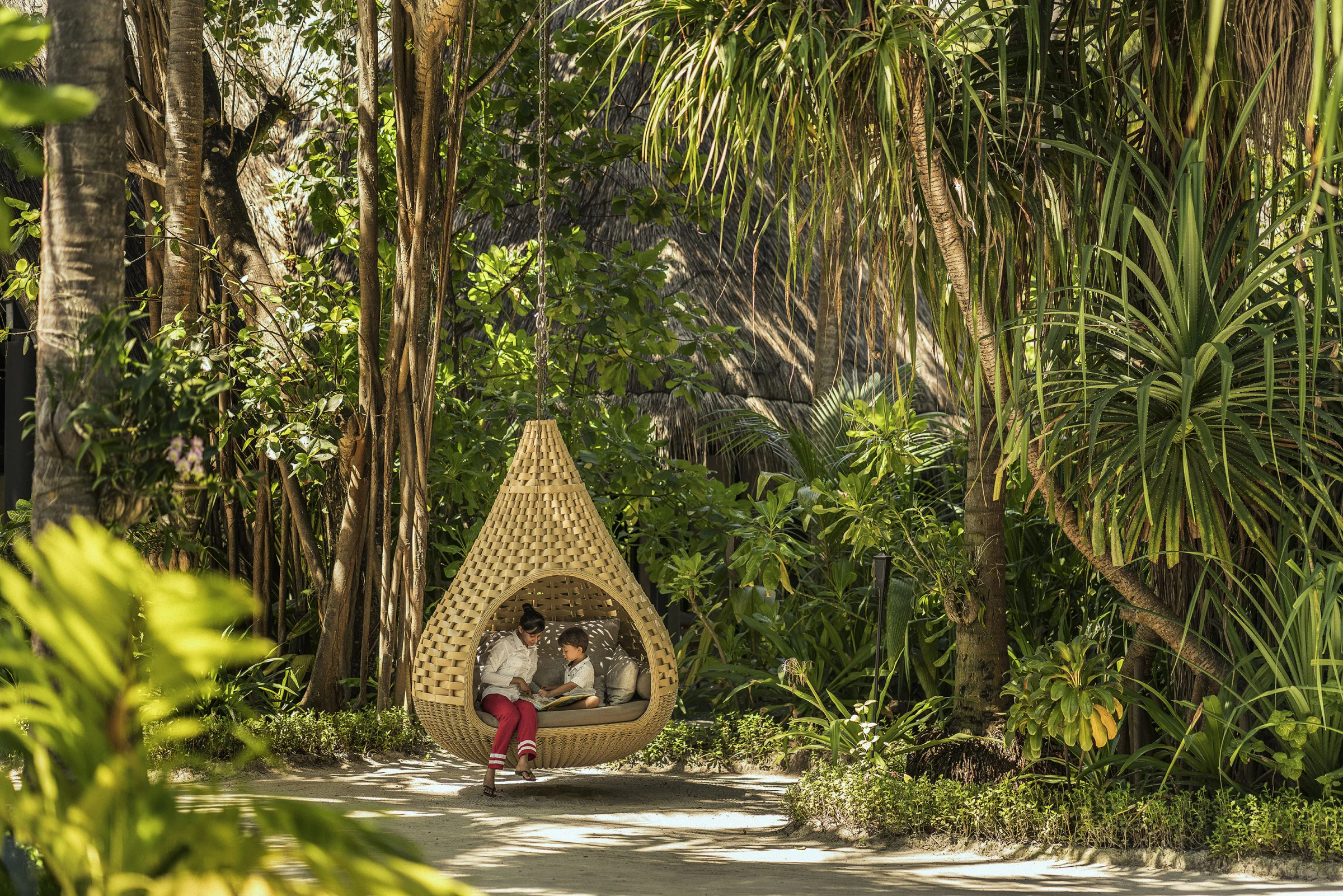 Child reading with a babysitter in a hanging garden chair, Anantara Kihavah