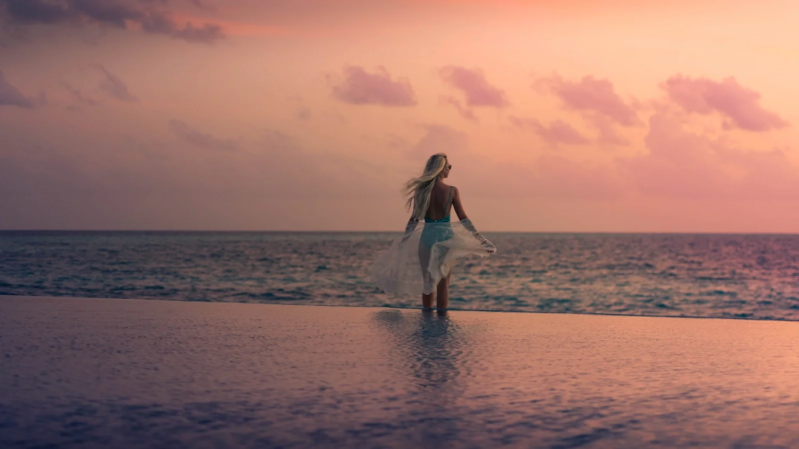 Woman at the infinity pool edge at sunset, Grand Park Kodhipparu