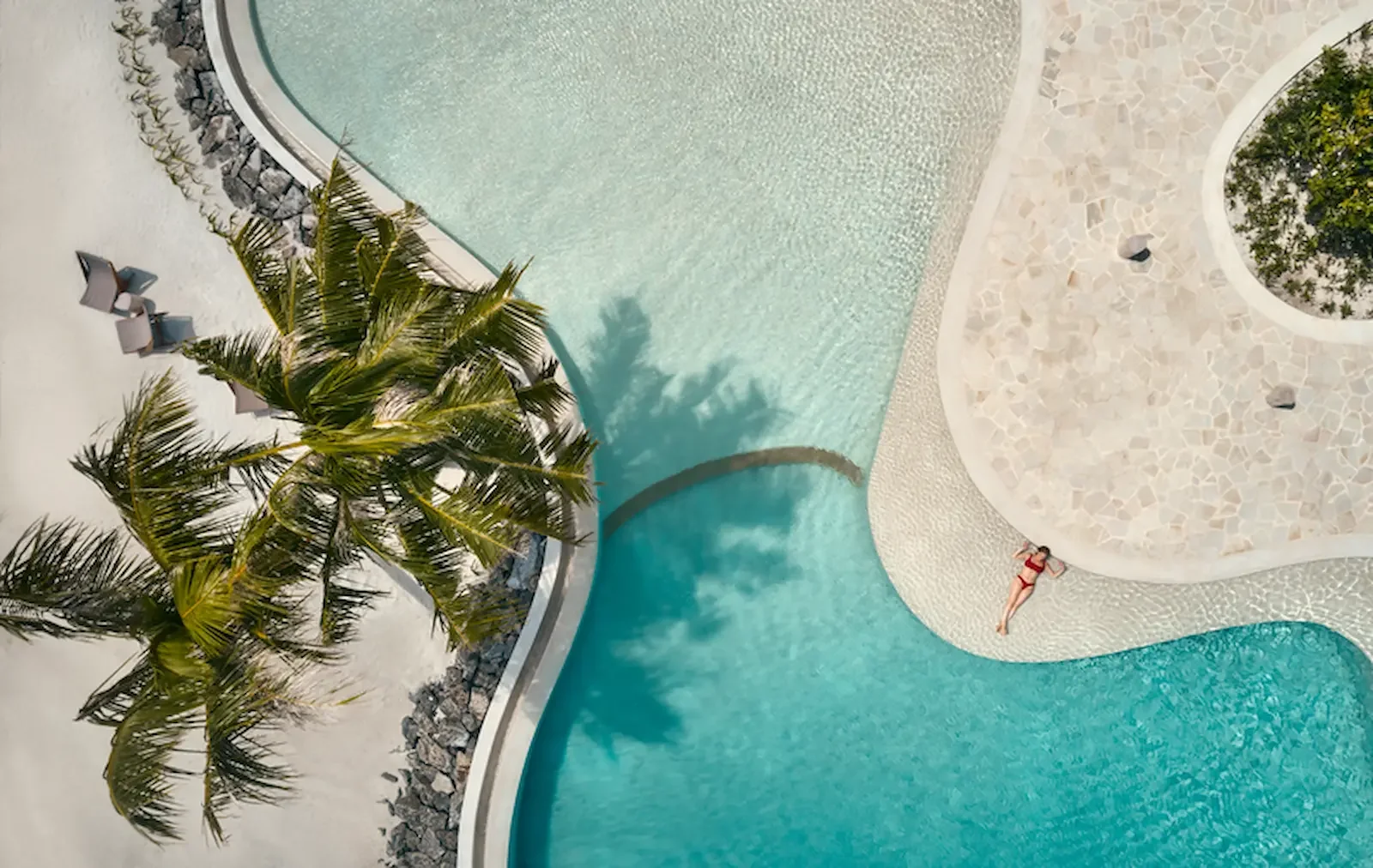 Guest by the lagoon pool beside the beach, Patina Maldives Fari Islands