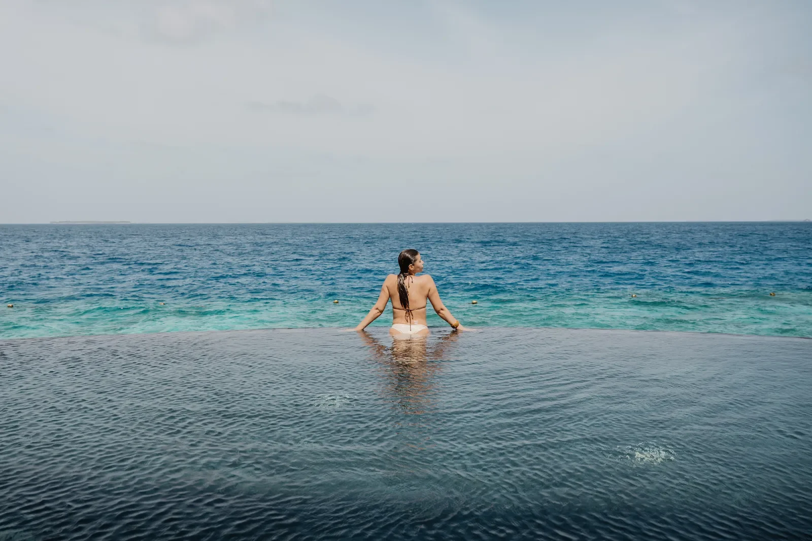 Woman in an infinity pool facing the ocean, Siyam World Maldives