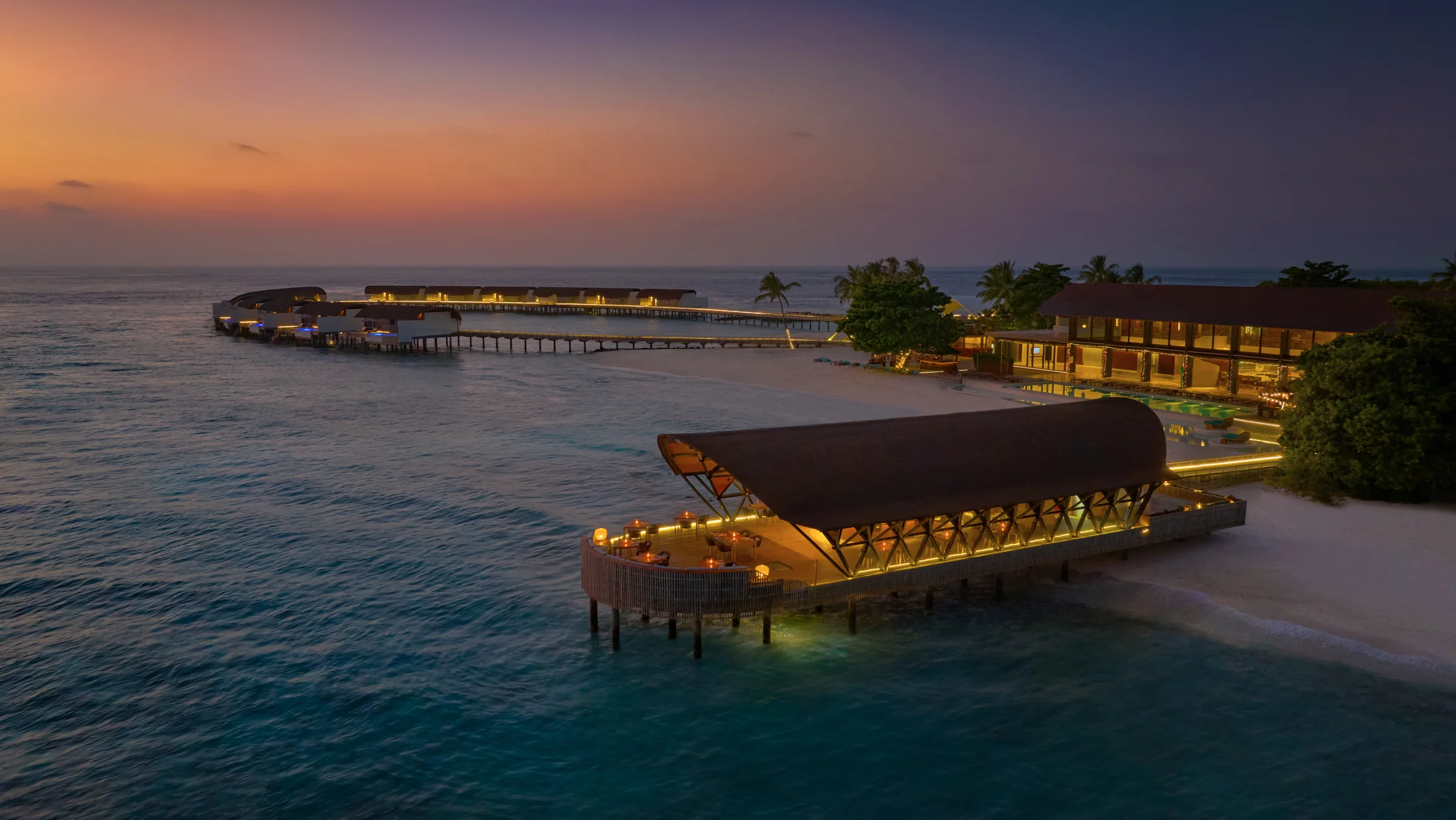 Overwater restaurant lit up at dusk, The Westin Maldives Miriandhoo Resort