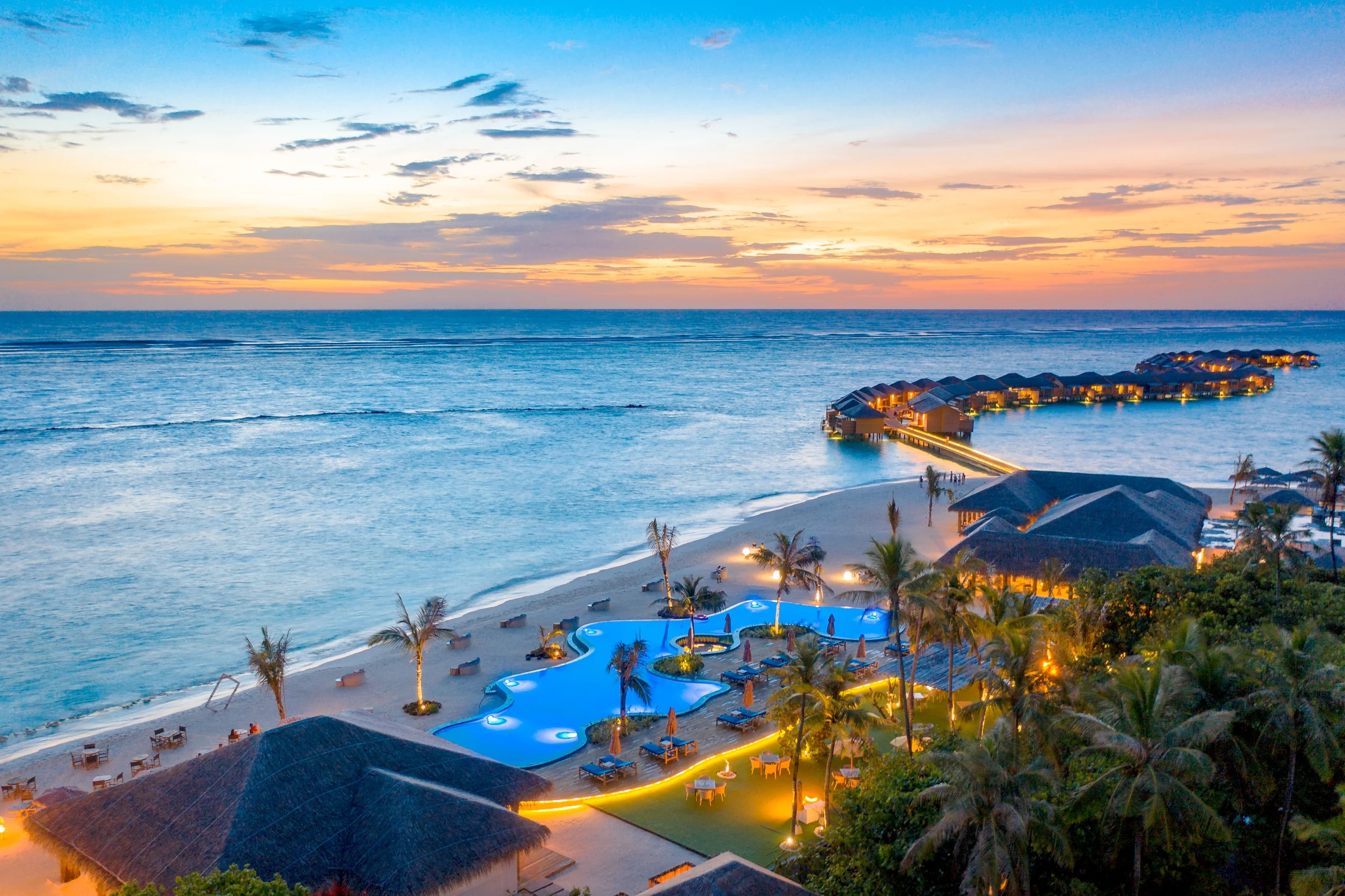 Pool and overwater villas lit up at dusk, You&Me by Cocoon